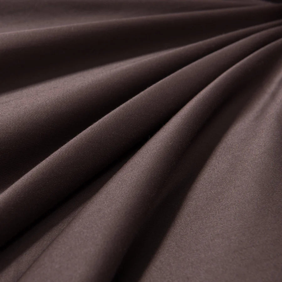 Organic cotton sheet set styled on bed in chocolate brown with linen throw