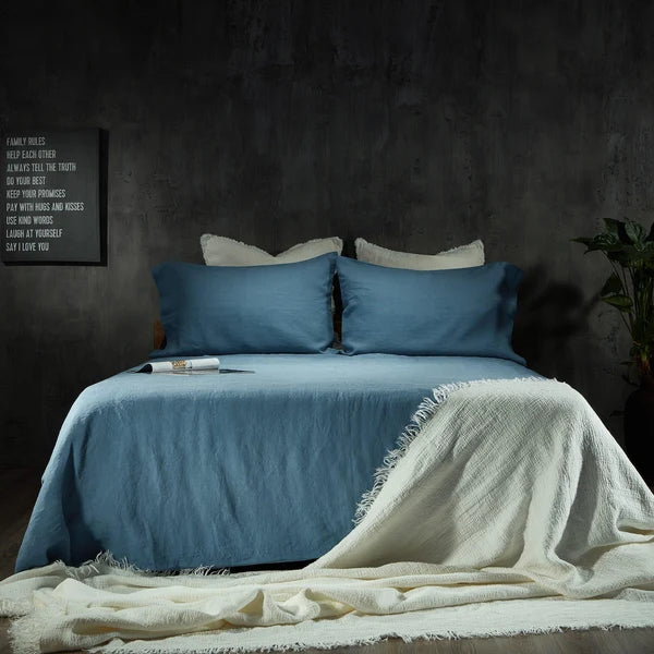 Aruba blue linen sheet set styled on bed with white fringe throw in dark moody bedroom