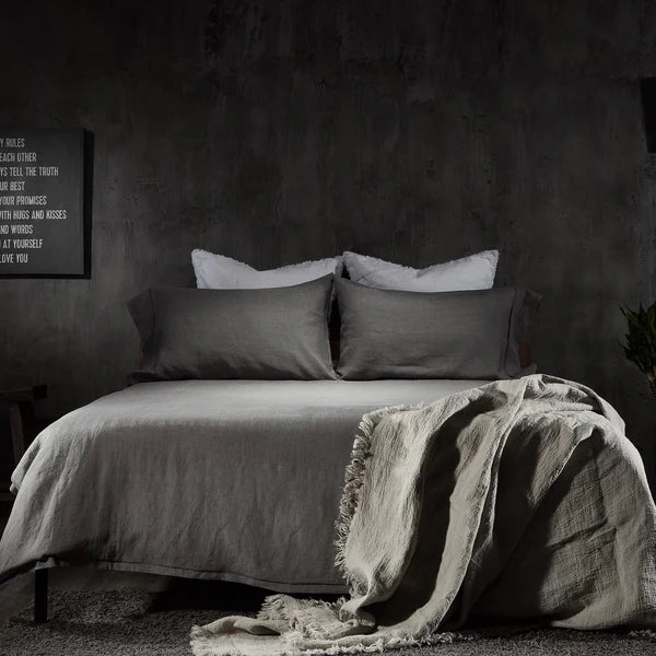 Charcoal linen sheet set styled on bed with white fringe throw in dark moody bedroom