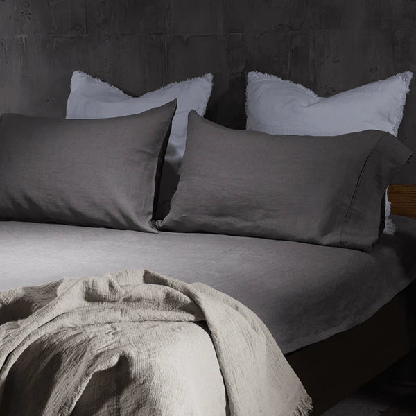 Charcoal linen pillowcases on bed with white fringe throw in dark bedroom
